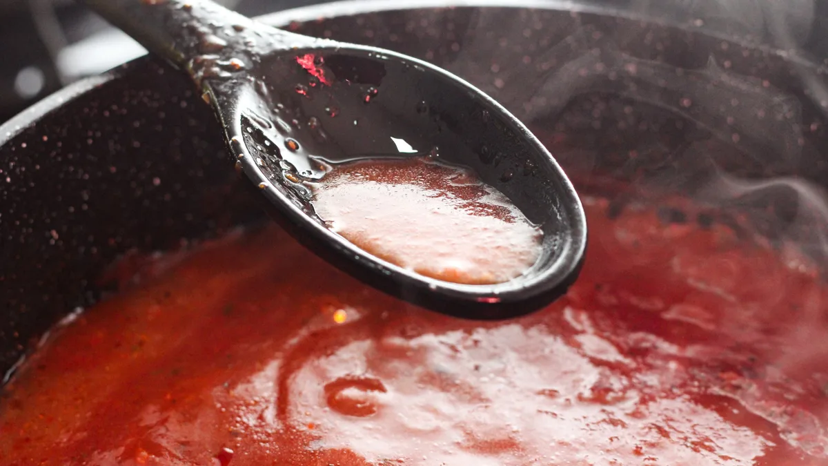 Sauce tomate maison dans une casserole, tomates fraîches, basilic et oignon sur un plan de travail en bois.